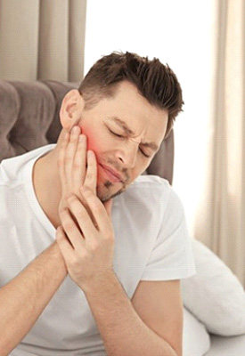 Man sitting in bed rubbing his aching jaw