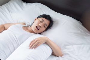 Woman snoring on white bed with sleep apnea