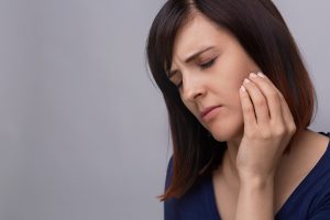 Woman on grey background holding fingers to jaw in pain