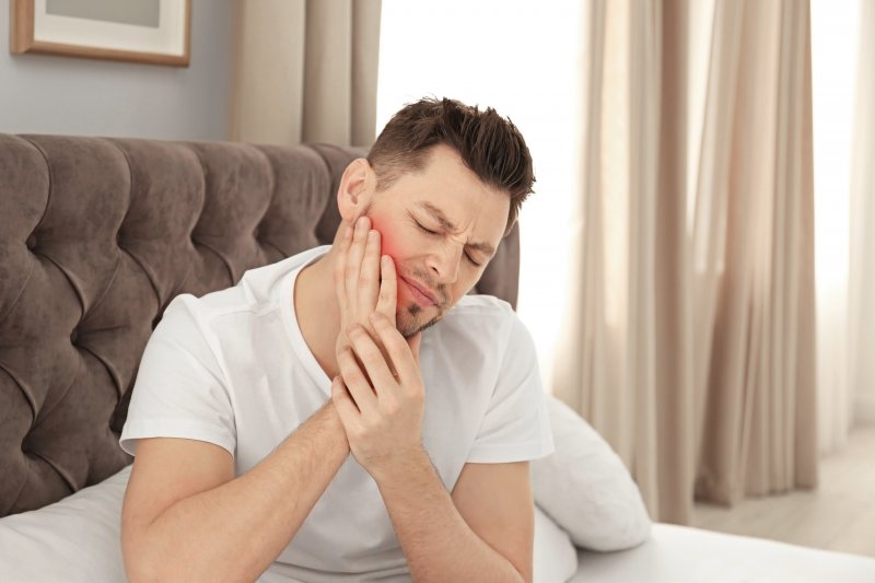 Man with TMJ and sleep apnea rubbing jaw in bed