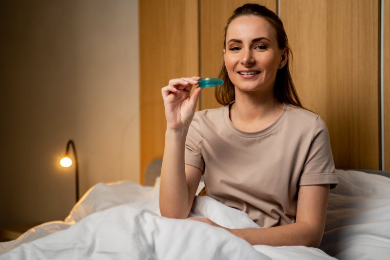 A woman sitting up in bed showing off her oral appliance