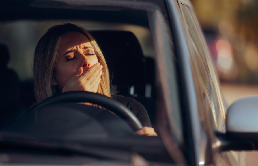 Woman yawning behind steering wheel